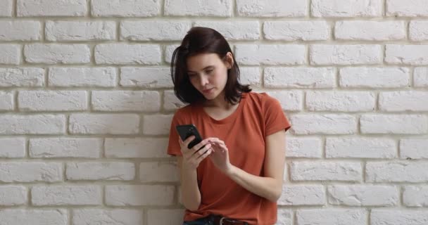 Chica con el teléfono móvil posando contra la pared de ladrillo fondo blanco — Vídeos de Stock