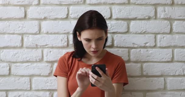 Flicka står inomhus hålla smartphone läsa otroliga nyheter känns glad — Stockvideo