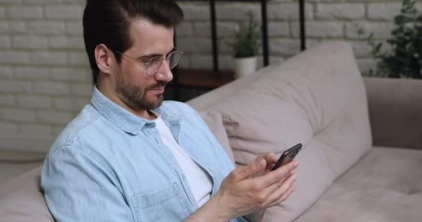 Homem sentar-se no sofá usar sorrisos smartphone mensagem de texto — Vídeo de Stock