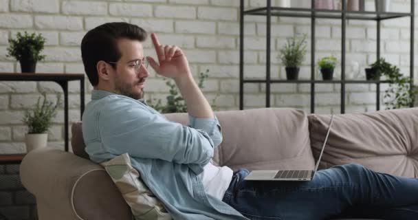 Man resting on couch using laptop chatting online — Stock Video