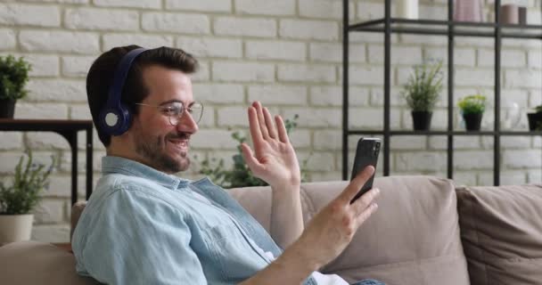 Guy usar fones de ouvido iniciar conversa videocall no telefone inteligente — Vídeo de Stock