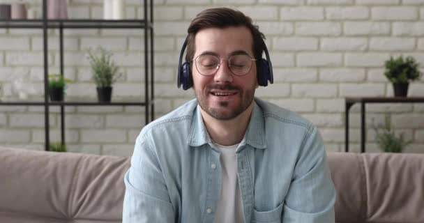 Ο άνθρωπος κάθεται στον καναπέ φορούν ακουστικά που εμπλέκονται στην επικοινωνία videocall — Αρχείο Βίντεο