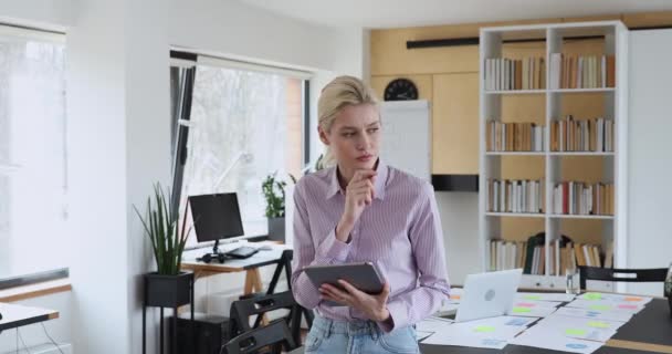 Umsichtige Mitarbeiterin steht im Büro und arbeitet an Tablet — Stockvideo