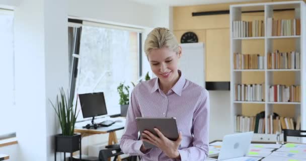 Приваблива жінка працює за допомогою планшета, стоячи в сучасній офісній кімнаті — стокове відео