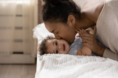 Şefkatli Afrikalı etnik kökenli anne küçük bir bebeğin yanağını öpüyor..