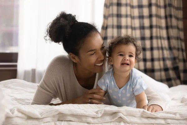 Affettuosa donna di razza mista sdraiata sul letto con bambino carino. — Foto Stock