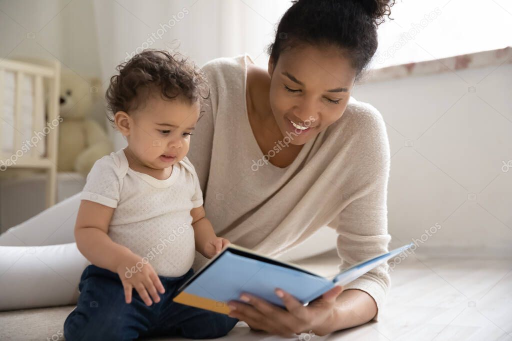 Caring young african woman reading fairy tale story to baby.