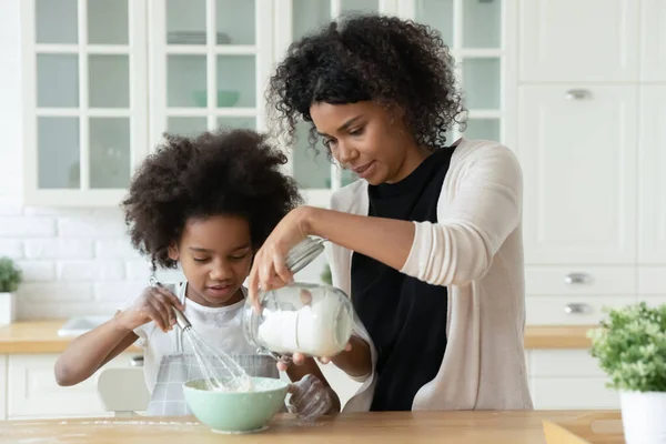 Cuidar a la joven madre afroamericana ayudando a la pequeña hija con la panadería. —  Fotos de Stock