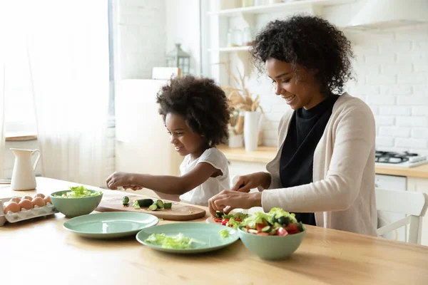 Sonriente joven africana etnia mujer cocina con su hija pequeña. —  Fotos de Stock