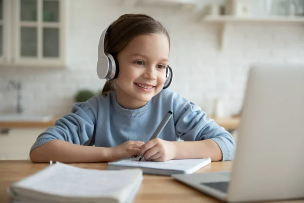 Feliz linda niña en los auriculares mirando la pantalla del ordenador portátil. — Foto de Stock