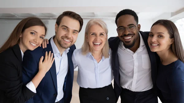 Portrait of smiling diverse colleagues hug posing in office