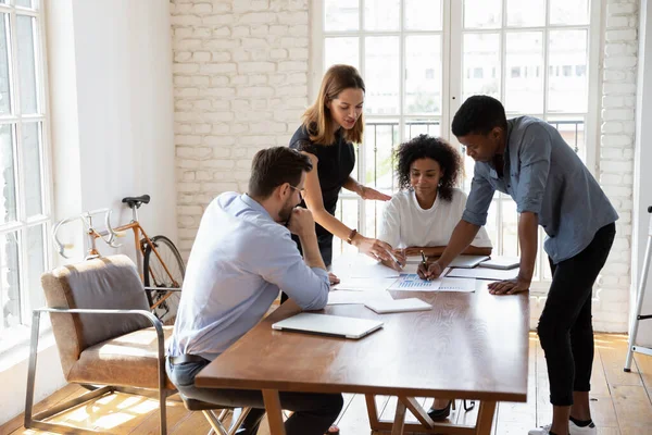 Diverse colleagues gather at desk discuss paperwork together