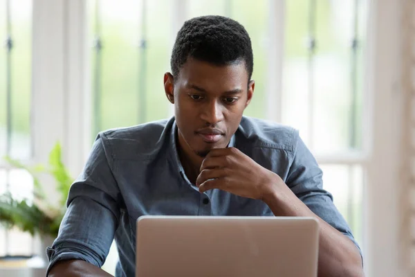 Pensive biracial male employee work on laptop thinking