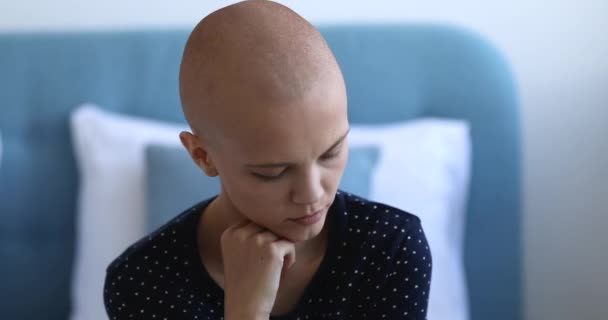 Женщина без волос после химиотерапии сидит в помещении, потерявшись от грустных мыслей — стоковое видео