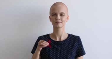 Kel kadın gri arka planda kırmızı farkındalık kurdelesi taşıyor