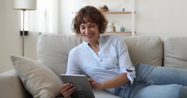 Mujer de mediana edad descansando en el sofá con el dispositivo de la tableta — Vídeos de Stock