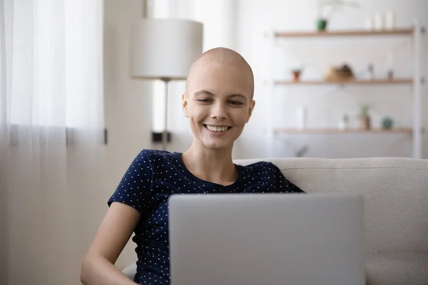 Smiling sick bald young woman relax browsing laptop