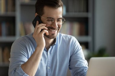 Gülümseyen genç adam müşteriyle telefonda konuşuyor.