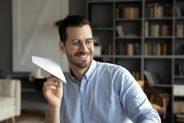 Smiling man have fun throwing paper plane at workplace