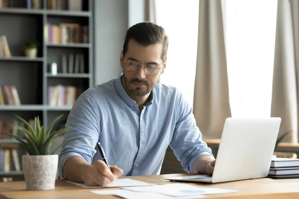 Junger Kaukasier macht sich Notizen am Laptop — Stockfoto