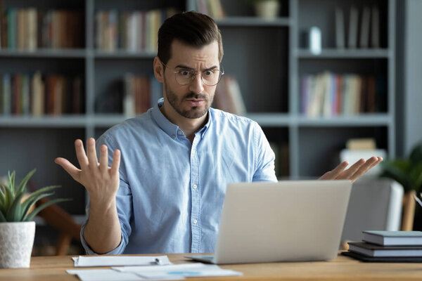 Unhappy young man work on laptop confused by gadget problems