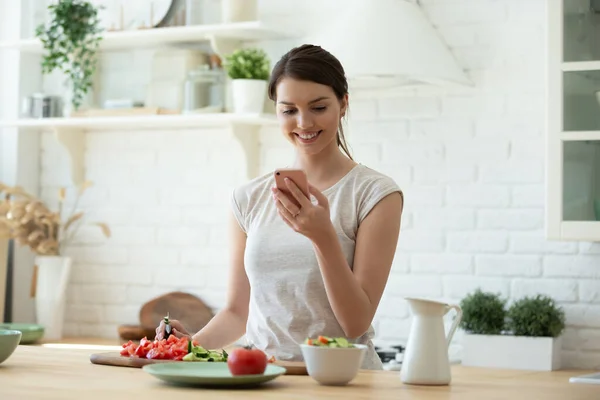 Young woman cooking and using mobile phone