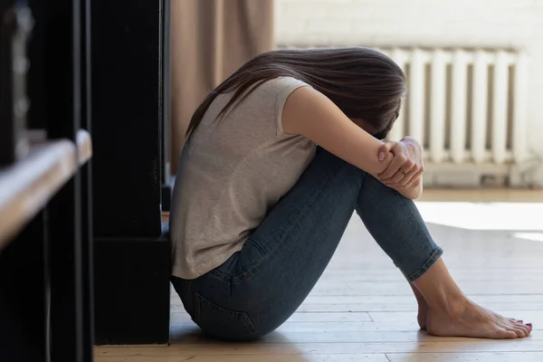 Mujer angustiada con los brazos alrededor de las rodillas sentada sola en el suelo — Foto de Stock