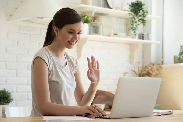 Genç bir kadın laptopta video görüşmesi yapıyor ve el sallıyor. — Stok fotoğraf