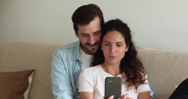 Çift, akıllı telefon kullanarak kanepede dinleniyor. İnternet eğlencesinin tadını çıkarıyor.
