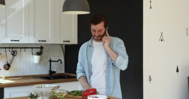 Mutfakta dikilmiş akıllı telefondan konuşan adamın yemek pişirmekten kafası karışmış.
