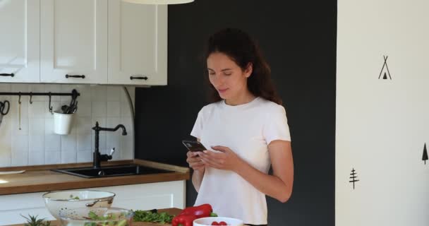 Женщина, стоящая на кухне использовать смартфон поиск вегетарианские рецепты — стоковое видео