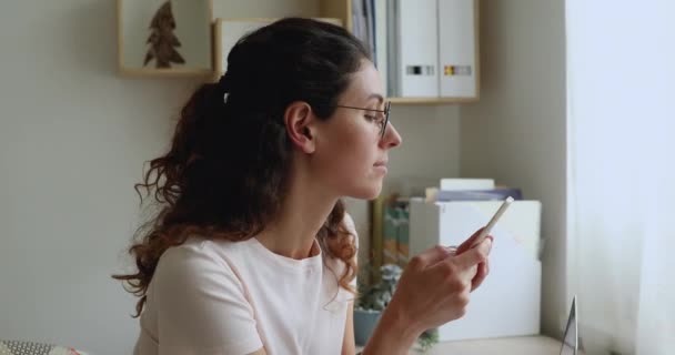 Женщина носит очки, держа смартфон с помощью поисковой информации в Интернете — стоковое видео