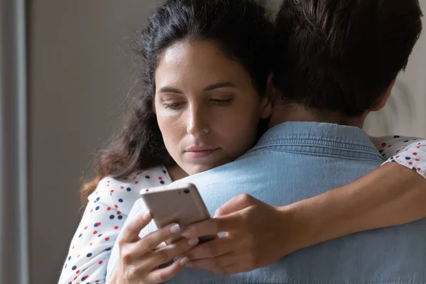 Junge Frau umarmt Ehemann beim Online-Betrug am Handy — Stockfoto