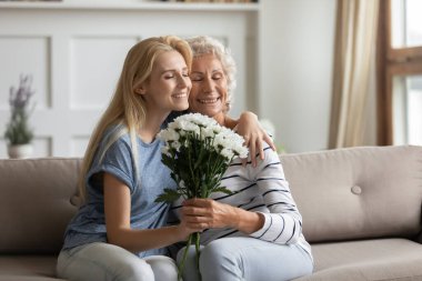 Sevecen yetişkin bir kız, yaşlı bir anneye sarılıyor ve tatille tebrik ediyor.