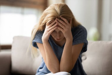 Bunalımlı genç bayan kanepede oturuyor, elleriyle başını sarıyor.