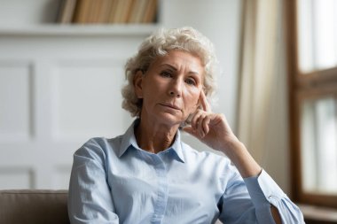 Kanepenin kırışık alnında poz veren sorunlu yaşlı kadın portresi.