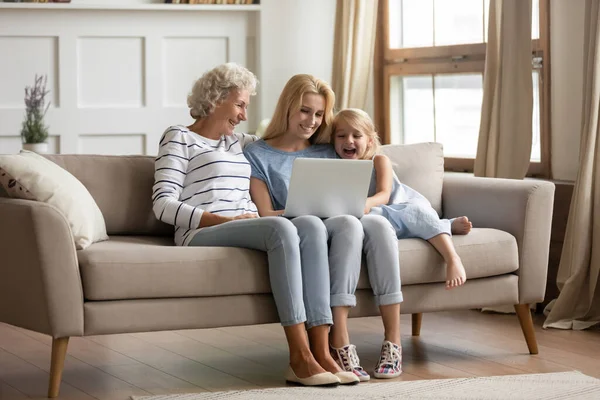 Familj till tre olika åldrar kvinnliga medlemmar vilar med bärbar dator — Stockfoto