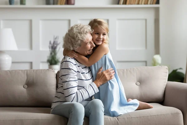 Adorable niña preescolar sosteniendo los brazos alrededor del cuello de la abuela madura —  Fotos de Stock