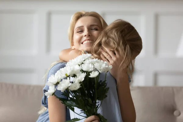 Emocionada mamá abrazando a su hijita recibiendo flores en el Día de las Madres —  Fotos de Stock