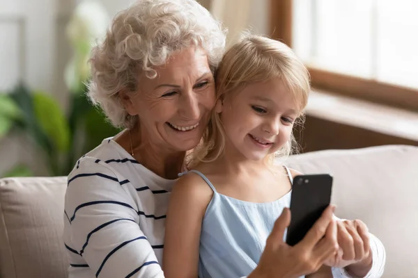 Glückliche Oma im Ruhestand und kleine Enkelin surfen per Handy im Internet — Stockfoto