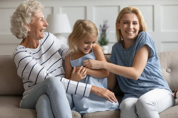 Lachen mama en oma kietelen met kleine meisje op de bank — Stockfoto