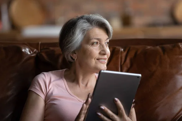 Smiling senior woman use tablet relaxing at home