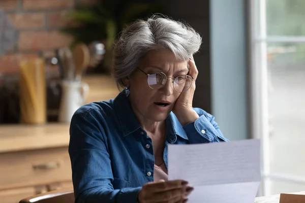 Unhappy senior woman shocked by bad news in postal correspondence