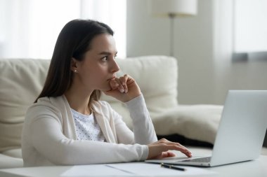 Düşünceli genç bir kadın dizüstü bilgisayar üzerinde çalışıyor.