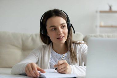 Genç kadın dizüstü bilgisayarda webinar izlerken not alıyor.