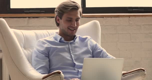 Guy sentar-se em poltrona usar laptop gastar tempo na internet — Vídeo de Stock