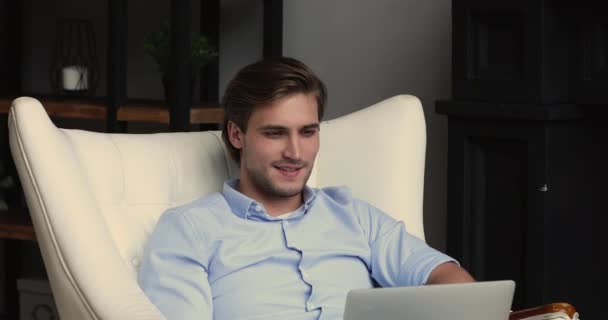 Jóképű srác sovány kényelmes puha bőr fotel laptoppal — Stock videók