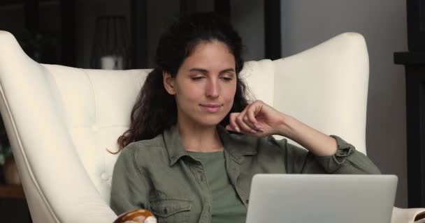 Mooie dromerige vrouw ontspannen in gezellige zachte fauteuil met laptop — Stockvideo