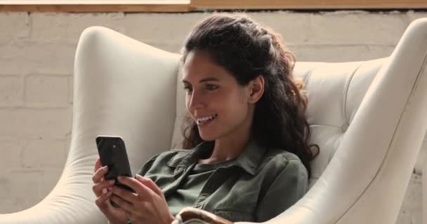 Vrouw zitten in fauteuil met smartphone lezen nieuws vieren succes — Stockvideo