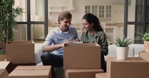 Счастливая пара распаковывает картонную коробку с вещами в день переселения — стоковое видео